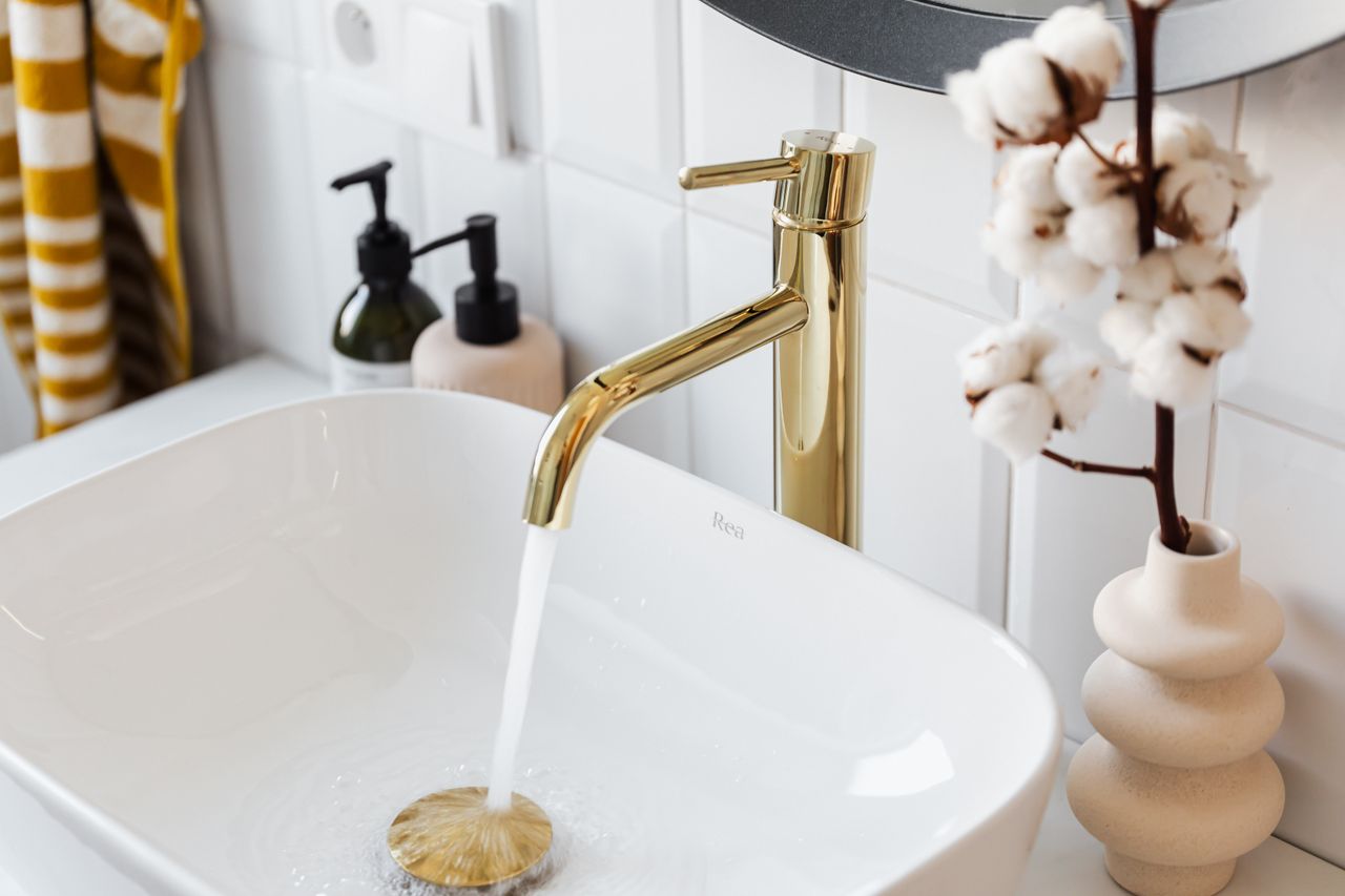 A stylish bathroom sink with a modern gold faucet and running water for a touch of luxury.